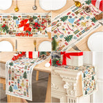 Cette image montre une belle décoration de table de Noël avec une nappe imprimée de motifs de sapin, de cadeaux et de personnages festifs, ainsi que d'autres éléments décoratifs comme des pommes de pin et des rubans rouges, le tout sur une surface en bois clair.