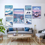 Des affiches de stations de ski dans un salon avec un canapé gris, une table basse en bois et des coussins bleus.