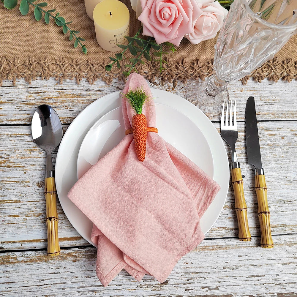 Sur une table en bois rustique, une élégante configuration de table de fête avec une nappe rose, des couverts dorés, une bougie et un bouquet de roses roses.