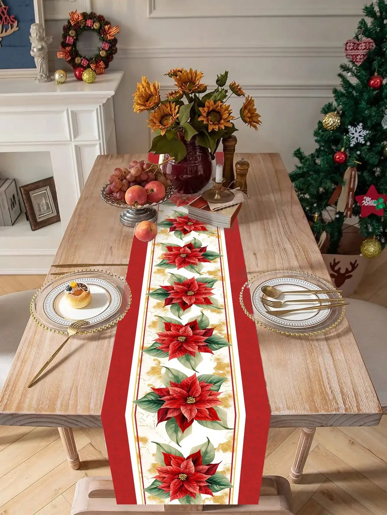 Une table décorée pour Noël avec un centre de table de fleurs d'automne, des fruits et une décoration festive, ainsi qu'un chemin de table orné de poinsettias rouges.