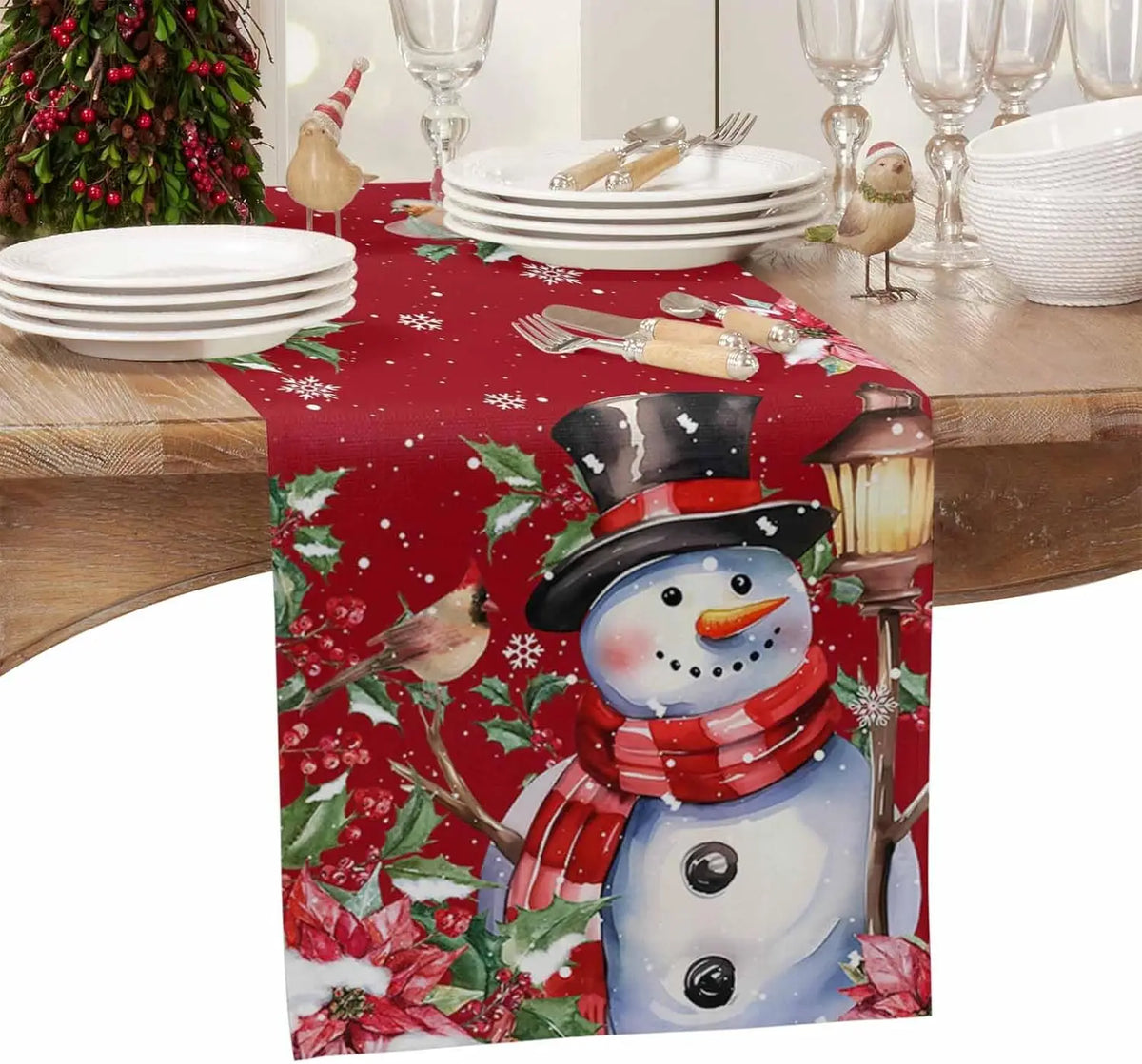 Une scène festive avec un bonhomme de neige souriant sur une nappe rouge décorée de motifs de houx et de flocons de neige, entouré d'assiettes, de verres et d'accessoires de table.