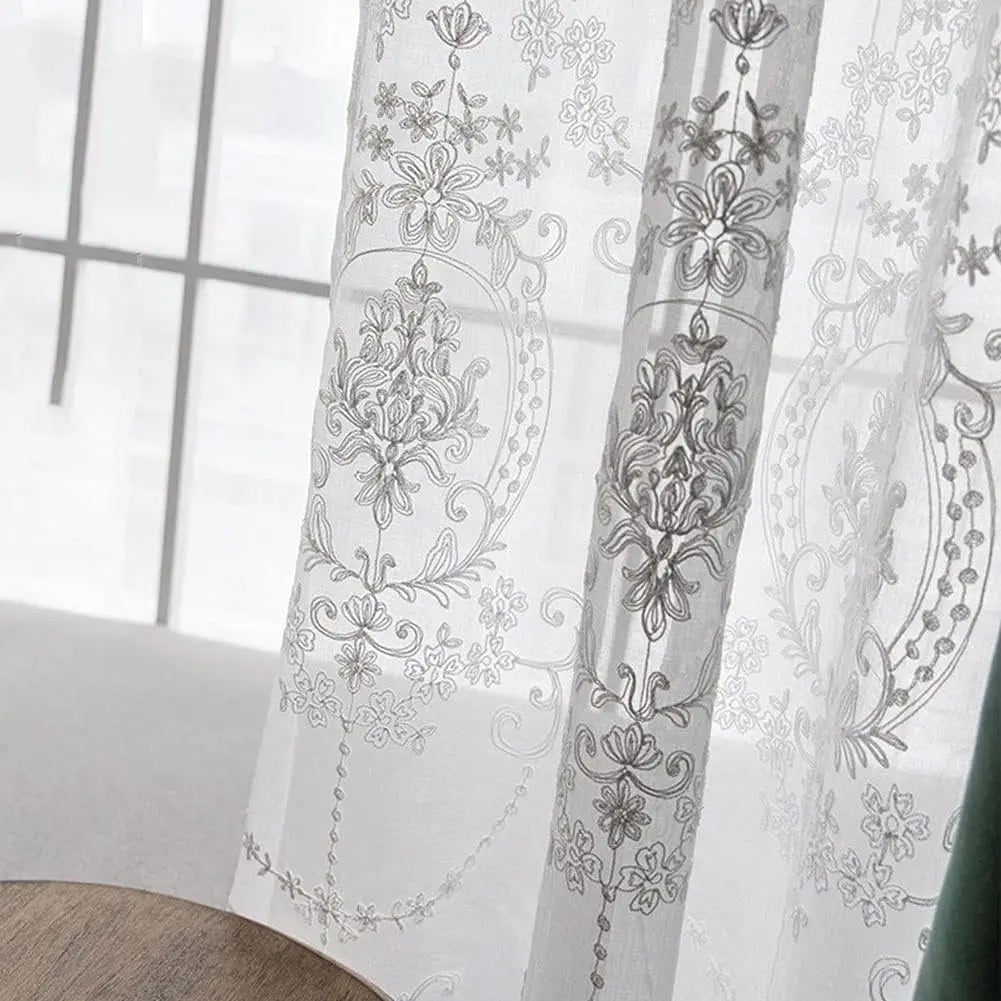 Gros plan sur les broderies florales d’un voilage blanc, laissant passer la lumière avec subtilité.
