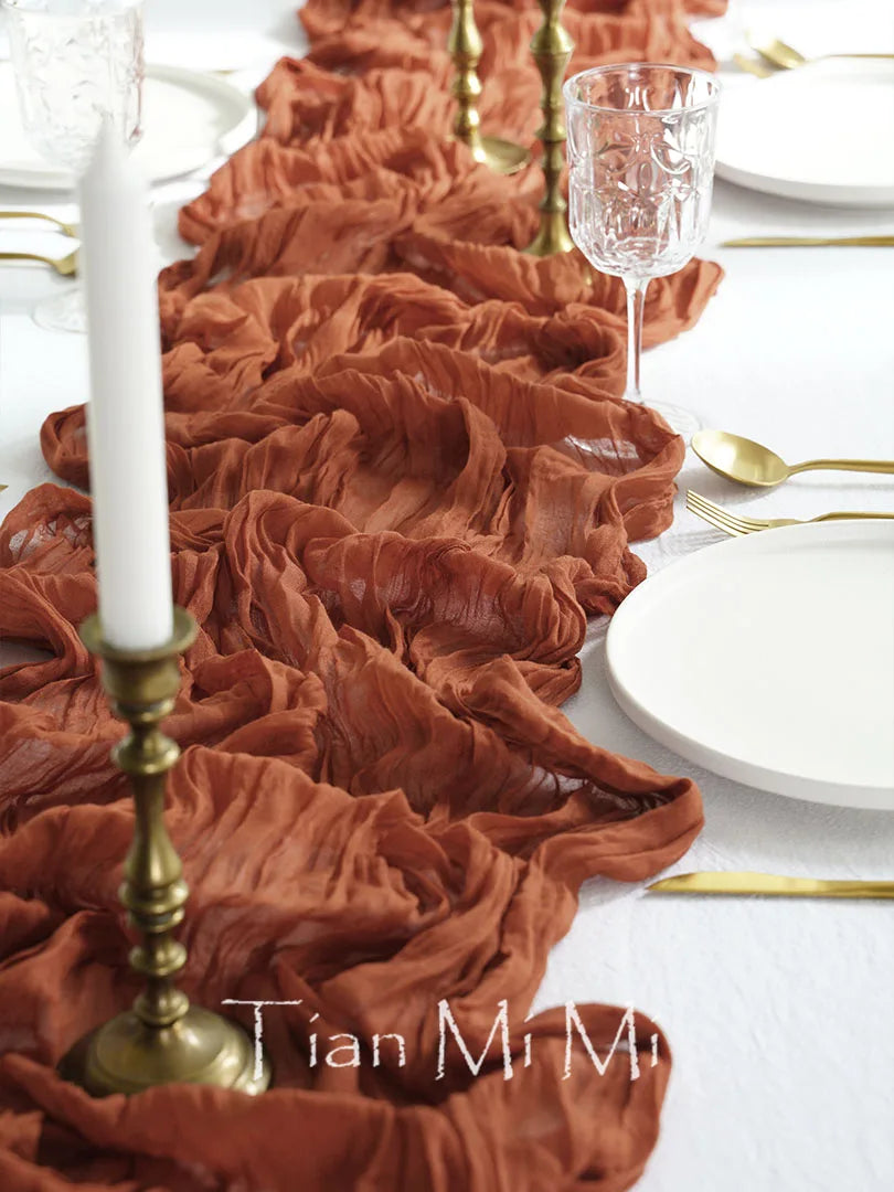 Cette image montre une élégante table de dîner dressée avec de beaux éléments décoratifs, notamment des bougeoirs dorés, des assiettes blanches et un chemin de table composé de fleurs orangées froissées.