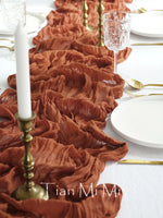 Cette image montre une élégante table de dîner dressée avec de beaux éléments décoratifs, notamment des bougeoirs dorés, des assiettes blanches et un chemin de table composé de fleurs orangées froissées.