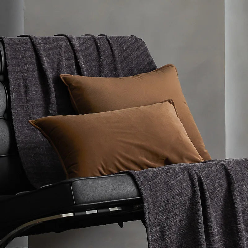 Fauteuil moderne avec coussins beiges et couverture grise, créant une ambiance confortable et élégante dans un intérieur épuré.