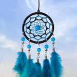 Capteur de rêves bleu et noir décoré de perles et de plumes sur fond de ciel bleu.