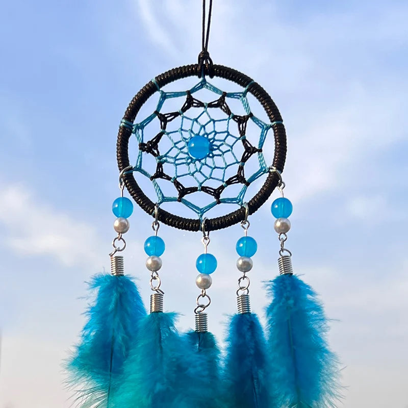 Capteur de rêves bleu et noir décoré de perles et de plumes sur fond de ciel bleu.