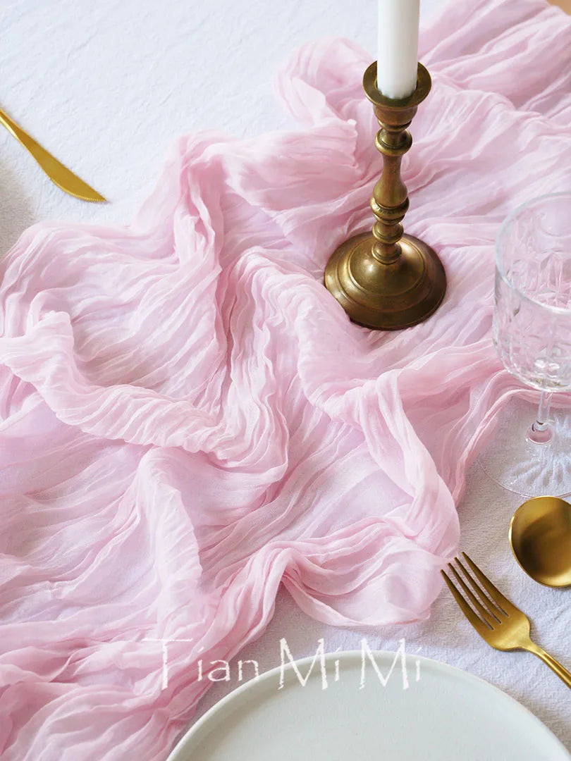 Composition élégante de table de décoration avec une nappe rose froissée et des accessoires dorés.