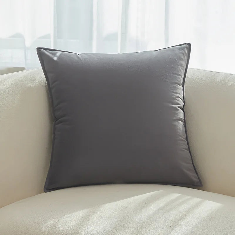 Coussin gris foncé sur un canapé blanc et crème près d'une fenêtre.