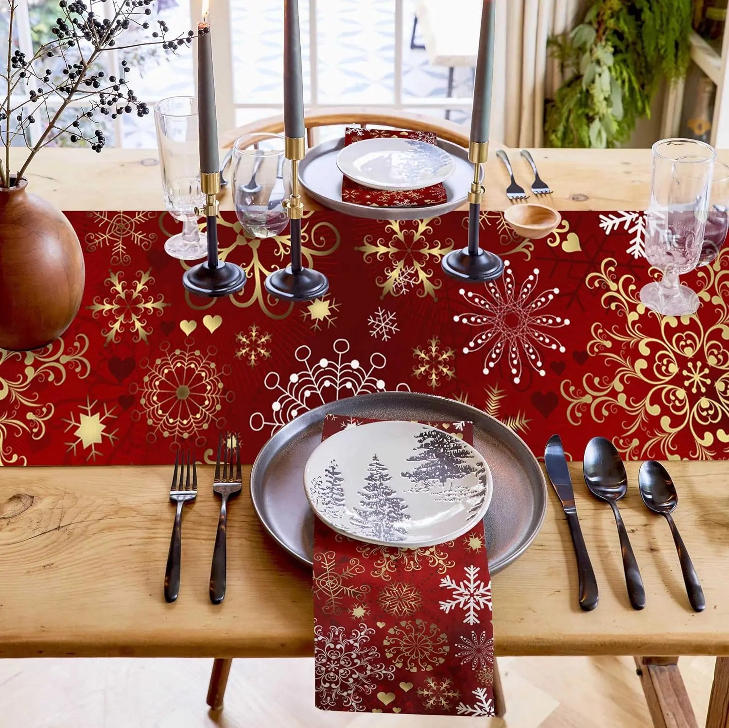 Table de fête élégante avec décoration de Noël rouge et or, comprenant assiettes, couverts, bougies et verres.