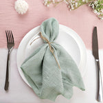 Une élégante table dressée avec des assiettes blanches, des couverts et une serviette de table verte nouée avec de la ficelle sur fond rose.
