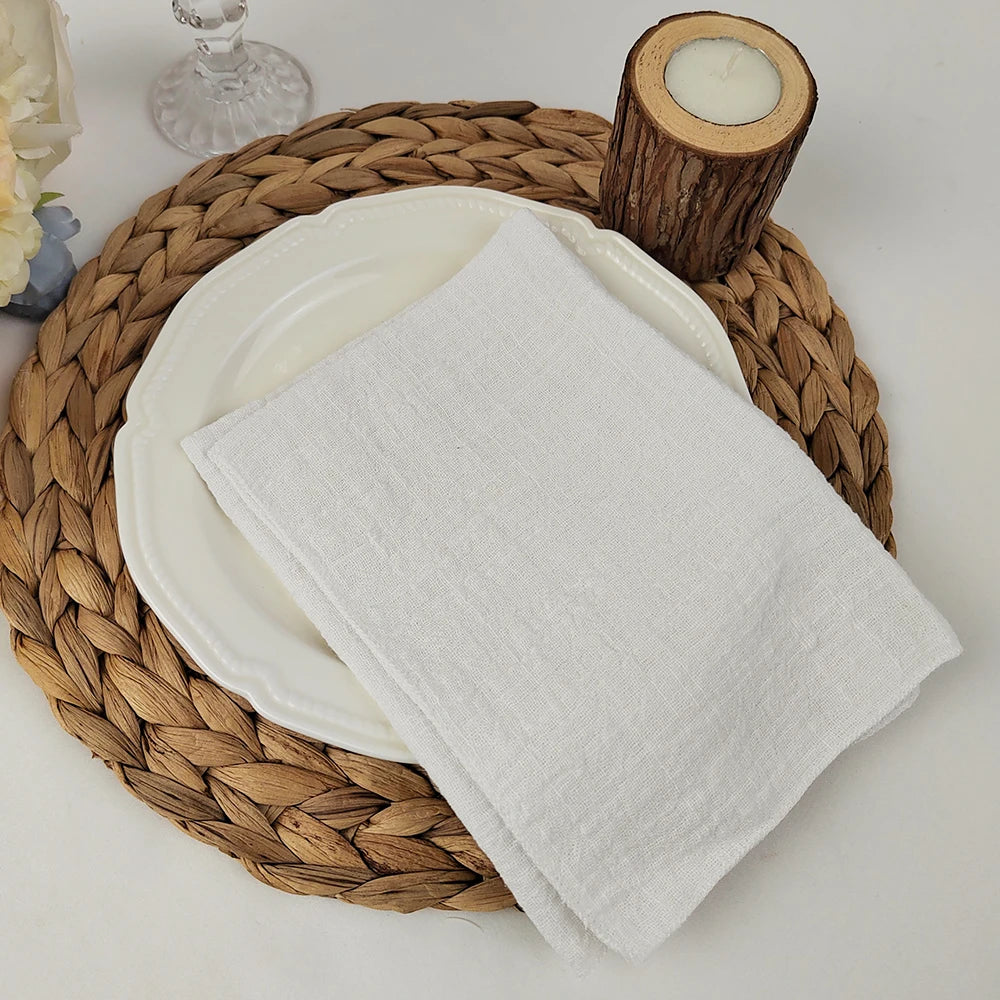 Des serviettes blanches reposent sur un napperon tressé en paille, avec un chandelier en bois sur le côté.