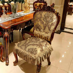 Chaise ancienne élégante au design baroque avec un revêtement tissu beige décoré de motifs floraux et d'ornements dorés, placée devant une table de style classique dans un intérieur luxueux.