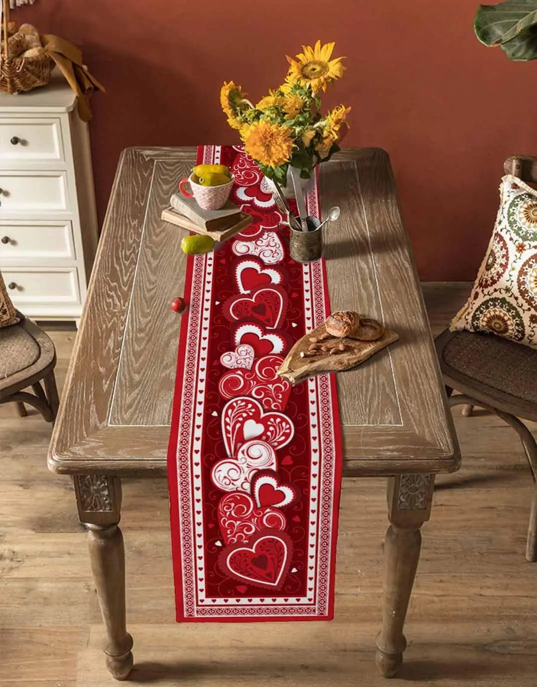 Table décorée d'un chemin de table rouge à motifs de coeurs et accents de tournesols, créant une ambiance romantique et chaleureuse pour un dîner ou un moment de détente.