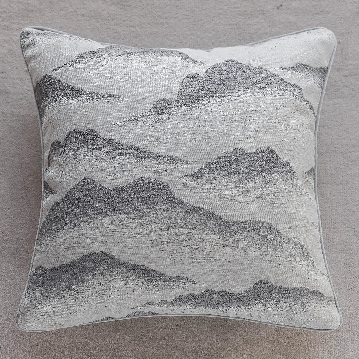 Coussin décoratif monochromatique à motif de paysage montagneux, avec des teintes de gris et de blanc.