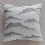 Coussin décoratif monochromatique à motif de paysage montagneux, avec des teintes de gris et de blanc.