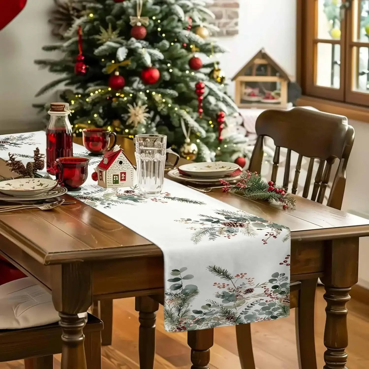 Table de Noël décorée avec un sapin illuminé, des verres et des accessoires dans des tons rouge et vert, donnant une ambiance chaleureuse et festive.