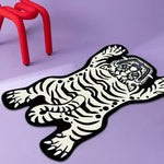 Un tapis de sol en forme de grand chat noir et blanc, avec des motifs et des textures très graphiques et stylisés, sur un fond violet.