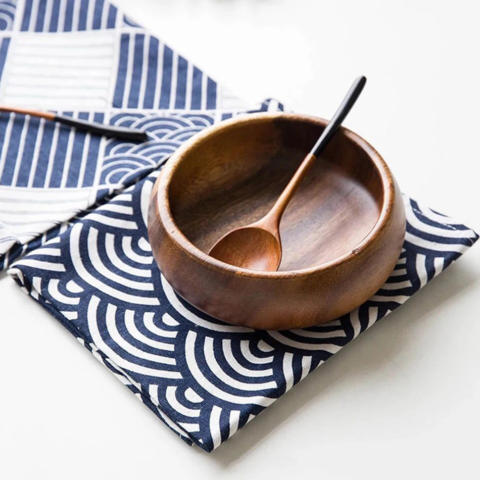 Un bol en bois avec des ustensiles en bois posé sur un tissu bleu et blanc motif graphique.