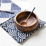 Un bol en bois avec des ustensiles en bois posé sur un tissu bleu et blanc motif graphique.