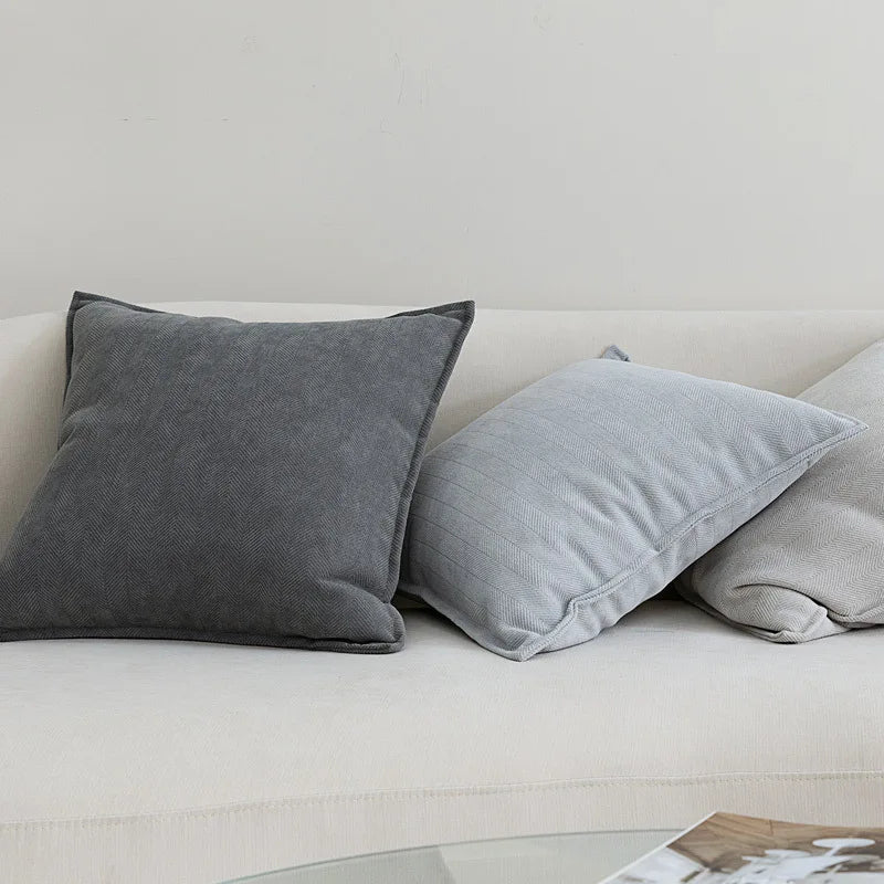 Gros plan sur des oreillers et coussins gris sur un canapé blanc, créant une atmosphère apaisante et élégante.
