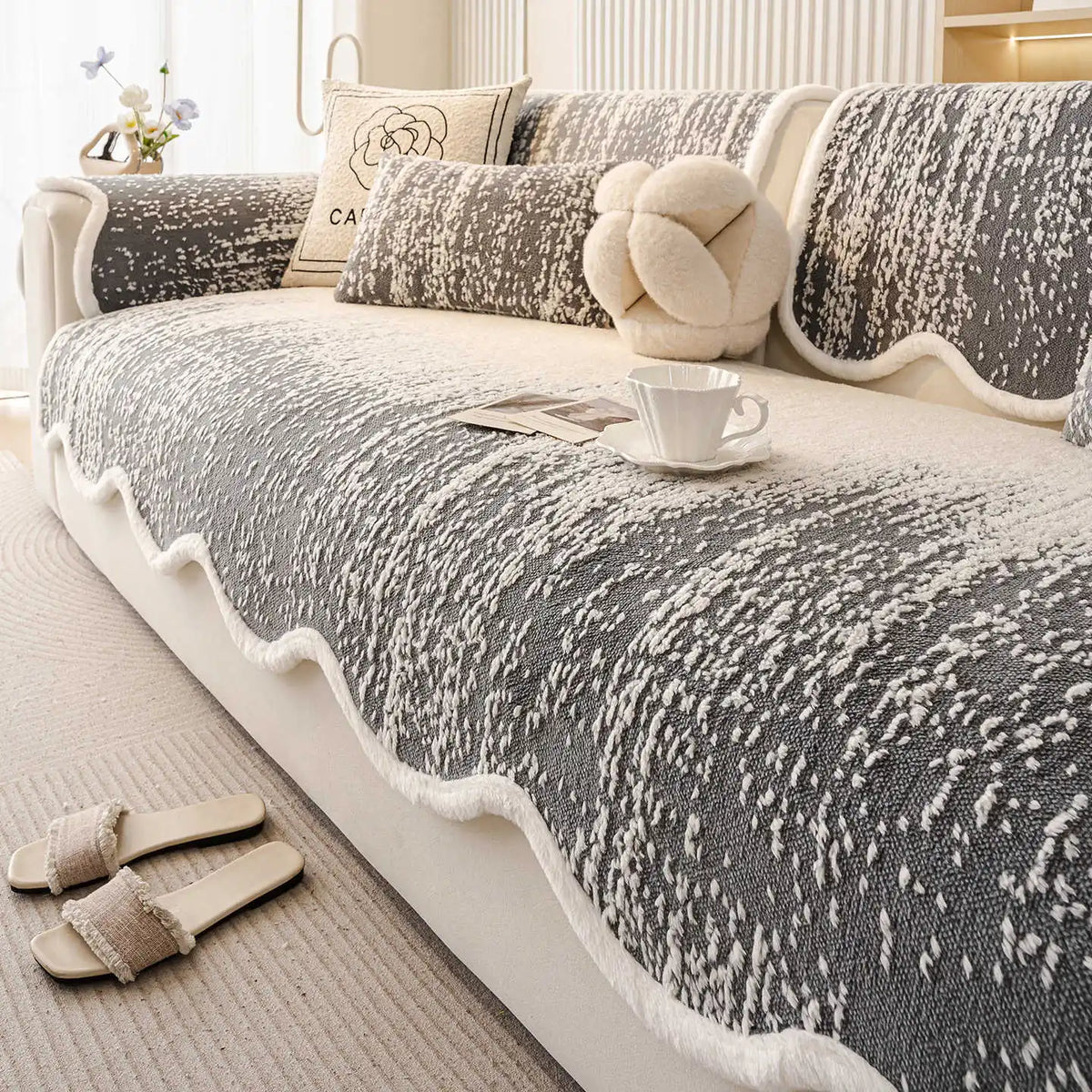 Un confortable canapé gris et blanc orné de coussins moelleux, avec une tasse de thé posée sur une petite table, créant une ambiance chaleureuse et apaisante.