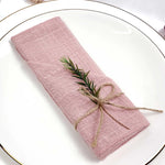 Un élégant tissu en lin rose pâle, enroulé et attaché avec de la ficelle, avec de petites branches de romarin disposées de manière décorative.