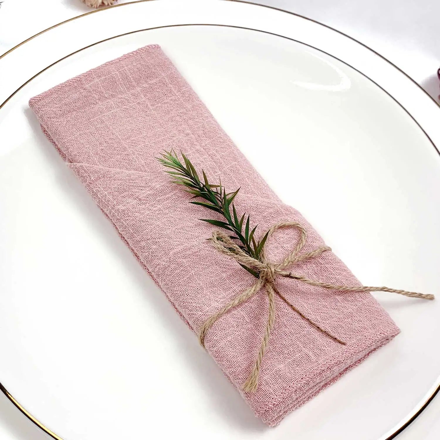 Un élégant tissu en lin rose pâle, enroulé et attaché avec de la ficelle, avec de petites branches de romarin disposées de manière décorative.