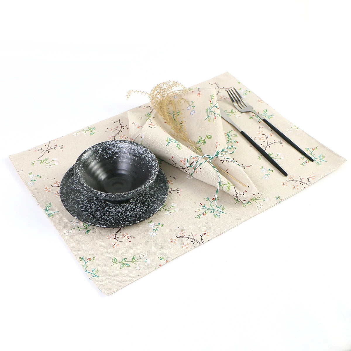 Assiette en pierre noire avec ustensiles sur un set de table fleuri beige.