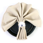 Un arrangement de serviettes beige élégantes enroulées autour d'une assiette noire sur fond blanc.
