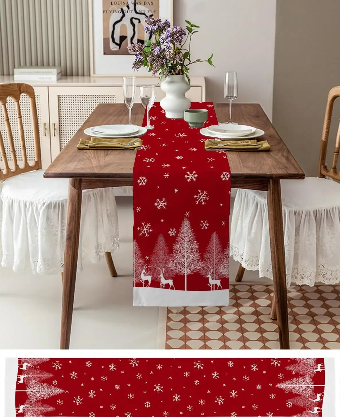 Une table joliment dressée avec des assiettes, des verres et une décoration de Noël, notamment un chemin de table rouge orné de motifs de flocons de neige et de silhouettes de cerfs.