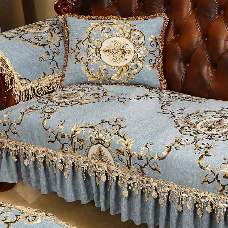 Taie de couette et coussin bleus ornés de motifs dorés floraux et de franges élégantes sur un canapé en cuir brun, créant une ambiance chic et luxueuse.