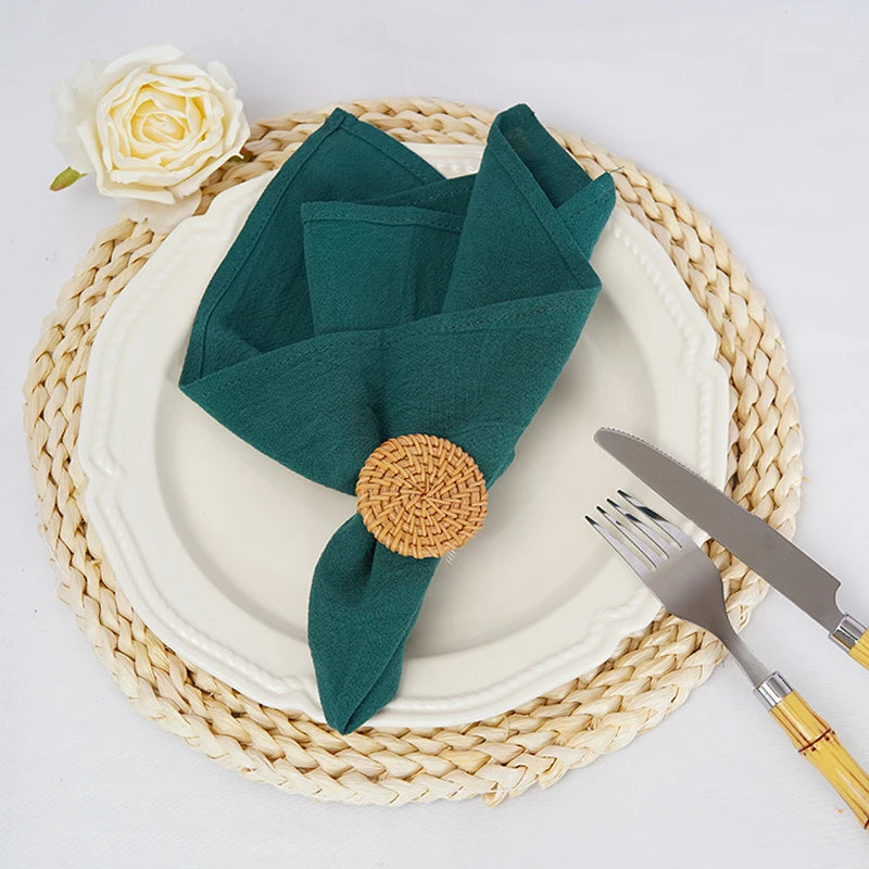 Cette image montre un ensemble de table composé d'une assiette blanche, de couverts dorés et d'une serviette de table pliée de couleur verte ornée d'un décor en rotin.
