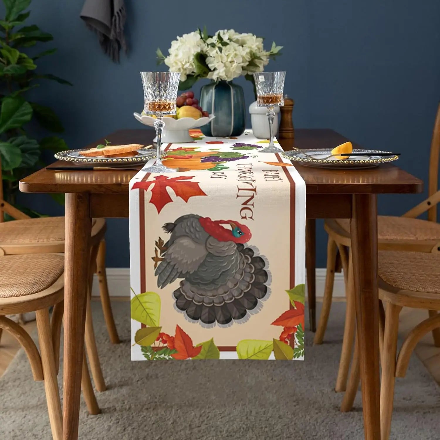 Cette élégante table de salle à manger présente une décoration automnale avec un chemin de table motif faune et flore, un bouquet de fleurs blanches et des accessoires de verre et de porcelaine, créant une ambiance chaleureuse et conviviale.