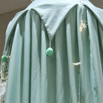 Ample robe de chambre moelleuse en vert pastel, avec des pompons en fourrure verte accrochés.