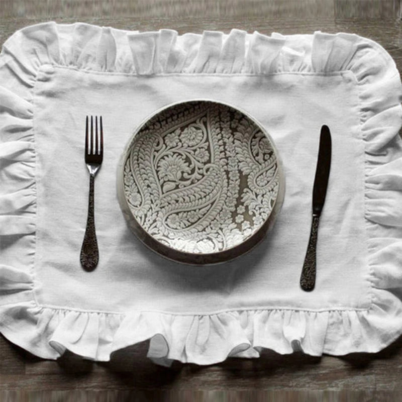 Une assiette décorative en porcelaine finement ciselée, entourée d'une nappe blanche ornée de volants, et accompagnée d'une fourchette et d'un couteau en métal.