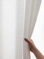 Voilage blanc texturé tenu par une main, en pleine lumière naturelle.