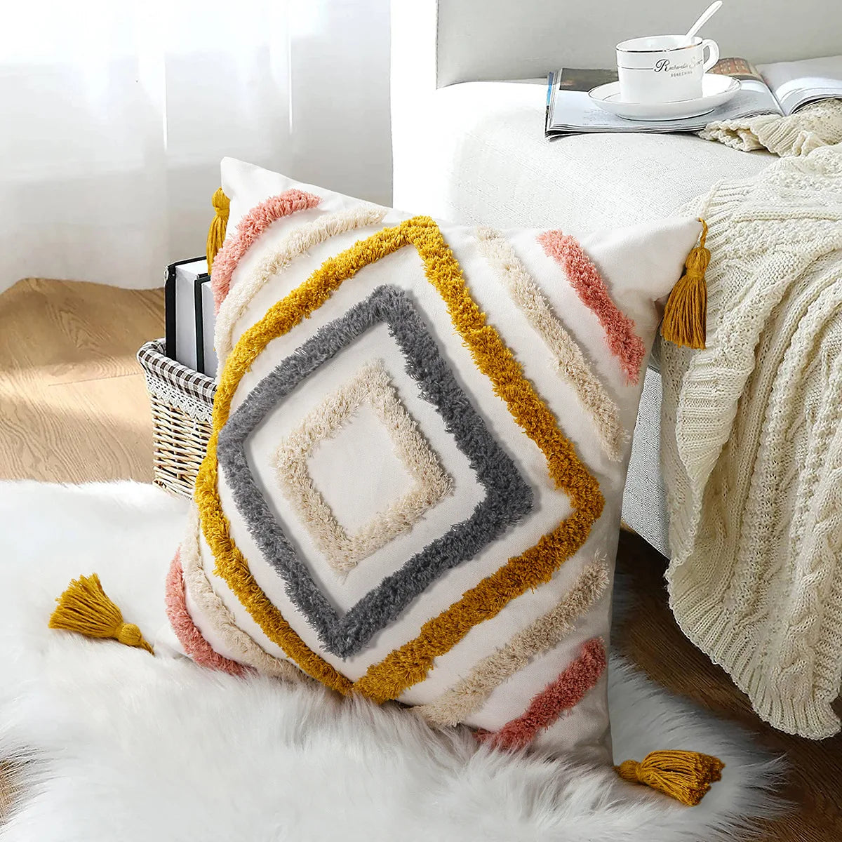 Coussin décoratif multicolore en peluche avec des franges et des glands, sur un lit douillet avec une couverture et un panier en osier.