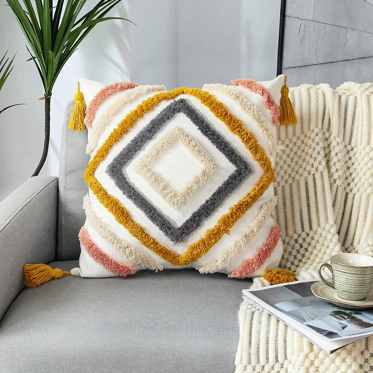 Coussin décoratif aux motifs géométriques aux couleurs chaudes et textures douces, placé sur un canapé gris dans un intérieur moderne avec plante verte.