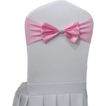 Une housse de chaise blanche dotée d'un nœud papillon rose avec un élément décoratif en strass au centre.