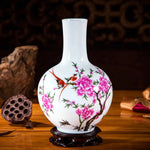 Vase en porcelaine blanche orné de fleurs de pivoine roses et d'oiseaux colorés, posé sur un support en bois sculpté.