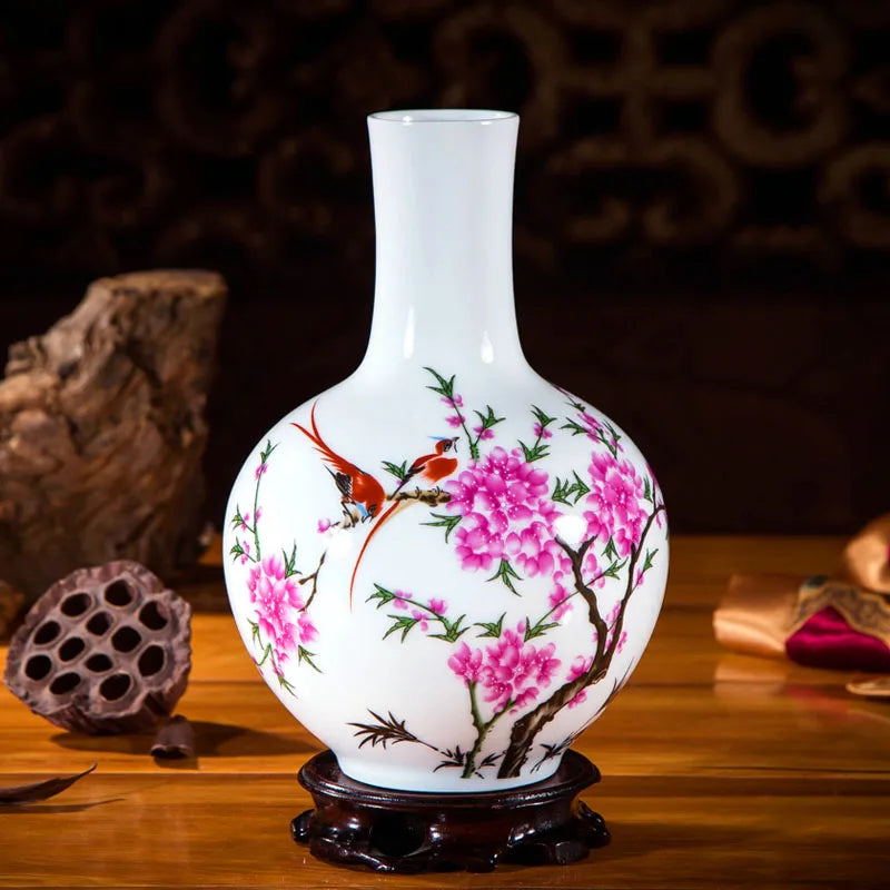 Vase en porcelaine blanche décoré de fleurs de pivoines roses et d'oiseaux colorés sur une branche, posé sur un socle en bois foncé.