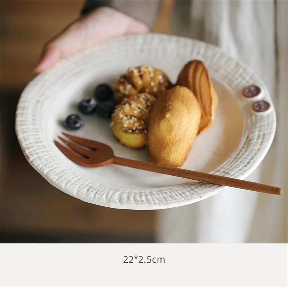 Sur une assiette blanche, on peut voir une pâtisserie doré ainsi que quelques baies bleues accompagnées d'ustensiles en bois.