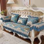 Un élégant canapé chesterfield blanc orné de coussins bleu-gris brodés de motifs floraux et de dentelle blanche, dans un salon de style classique.