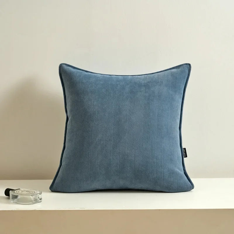 Coussin décoratif gris foncé en texture de chevrons sur une étagère blanche avec accessoires.