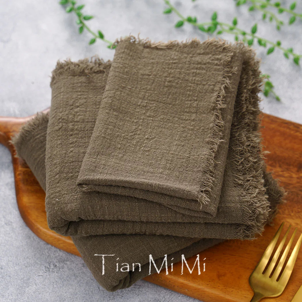 Des serviettes de table en lin marron foncé pliées sur un plateau en bois, avec le logo "Tian Mi Mi" imprimé.