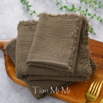 Des serviettes de table en lin marron foncé pliées sur un plateau en bois, avec le logo "Tian Mi Mi" imprimé.