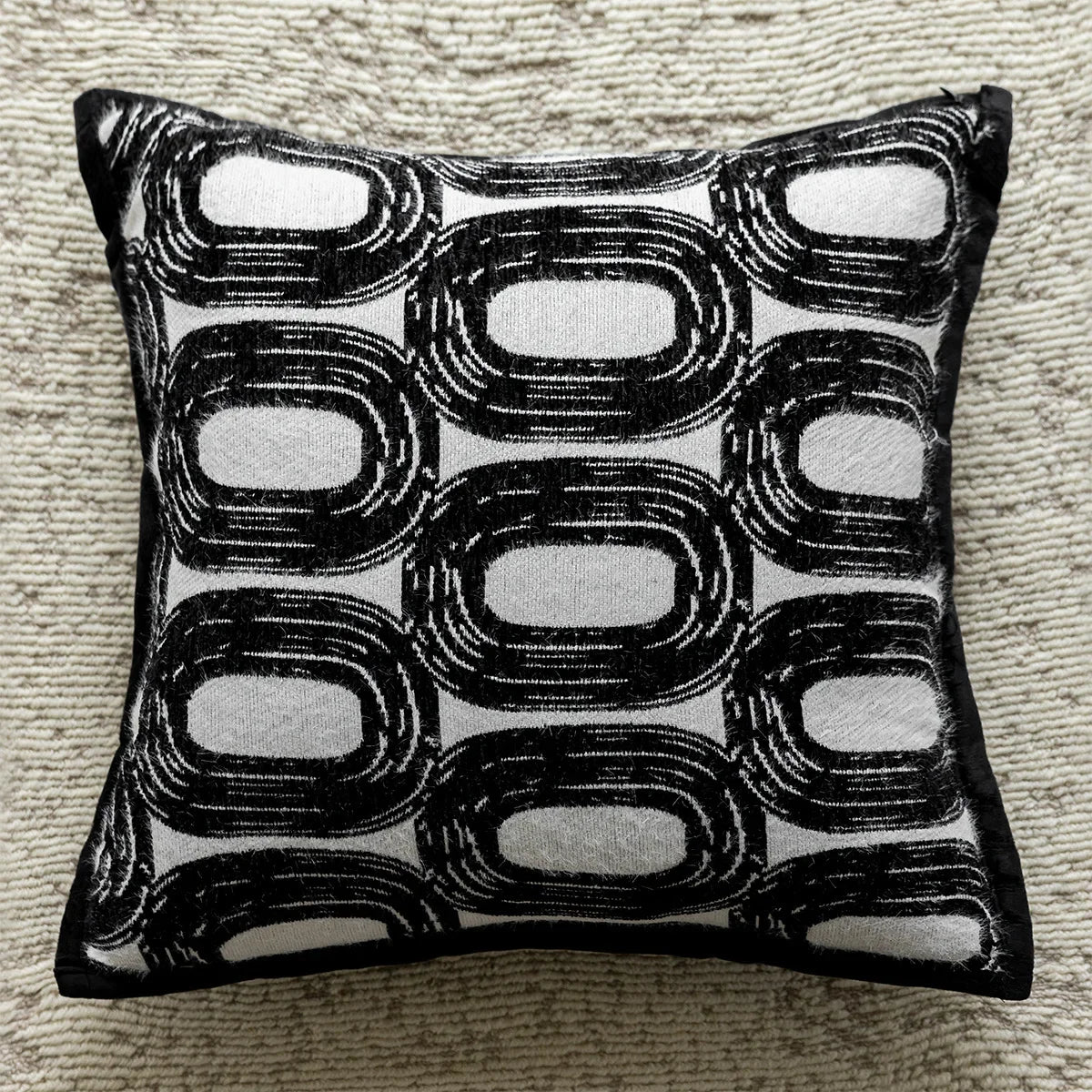 Coussin décoratif avec motif graphique en noir et blanc, composé de formes ovales répétées.
