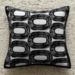 Coussin décoratif avec motif graphique en noir et blanc, composé de formes ovales répétées.