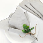 Serviette en lin grise avec un bouquet de feuilles vertes attaché avec de la ficelle de jute, sur une assiette blanche.